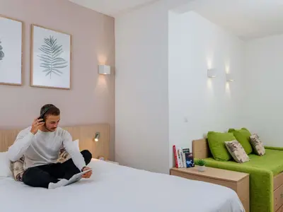 a person sitting on a bed talking on a cell phone at Aparthotel Adagio Access Bruxelles Europe Aparthotel in Brussels