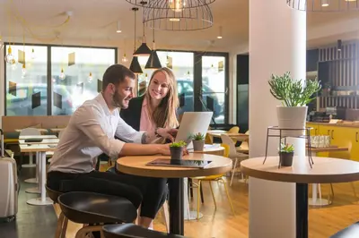 two people sitting at a table with a laptop at Aparthotel Adagio Access Bruxelles Europe Aparthotel in Brussels