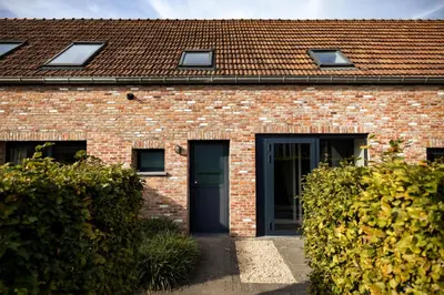 a brick house with a black door and two bushes at B&B Ginnekenshoeve in Beerse