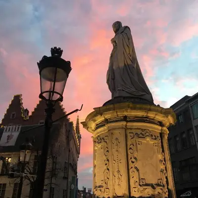 a statue and a street light with a sunset at Margaretha's Room in Mechelen