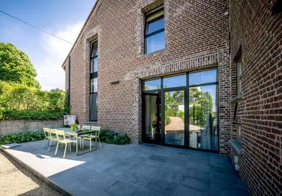 a patio with a table and chairs next to a brick building at B&B De Woestijn in Roosdaal