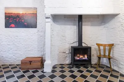 a fireplace in a room with a chair and a table at Romantic 16th century workers house in Ghent