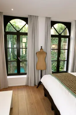 a bedroom with large windows and a bed and a table at Coeur Sablon in Brussels