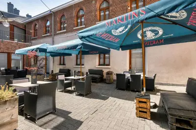 a patio with tables and chairs and blue umbrellas at Martin's Patershof in Mechelen