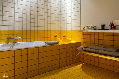 a yellow tiled bathroom with two rubber ducks on a tub at B&B La Corderie in Hamme