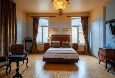 a bedroom with a bed and a chair and windows at Charme Hotel Hancelot in Ghent