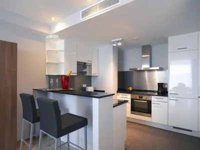 a kitchen with white cabinets and a bar with stools at Thon Residence Florence Aparthotel in Brussels