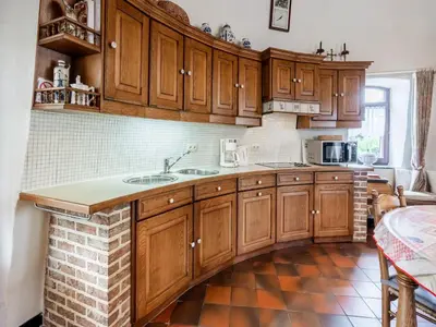 a kitchen with wooden cabinets and a brick floor at Charming Nieuwpoort Mill Retreat in Zottegem
