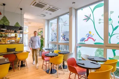 a man walks through a restaurant with tables and chairs at B&B HOTEL Brussels Centre Gare du Midi in Brussels