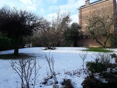 a snow covered yard with a building and trees at Un grand jardin en ville. Chez Guy in Brussels