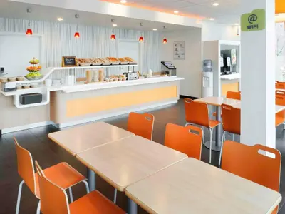 a fast food restaurant with tables and orange chairs at ibis Budget Brussels South Ruisbroek in Ruisbroek