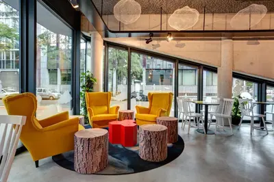a lobby with yellow chairs and tables and windows at MEININGER Hotel Bruxelles Gare du Midi in Brussels