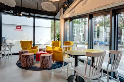 a cafe with yellow chairs and tables and windows at MEININGER Hotel Bruxelles Gare du Midi in Brussels