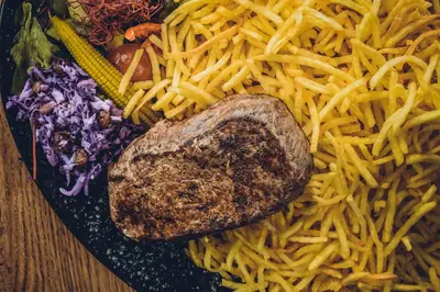 a plate of pasta with a piece of meat and vegetables at Hotel Colonie 7 in Merksplas