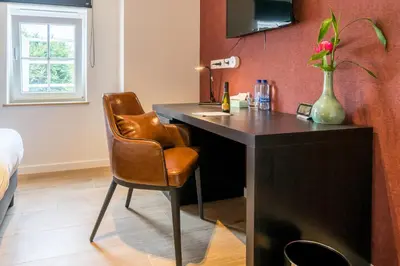 a desk with a chair and a vase with a flower at Hotel Huron in Mol