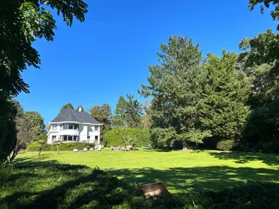 a white house on a green field with trees at B&B Des Heures Claires in Lasne