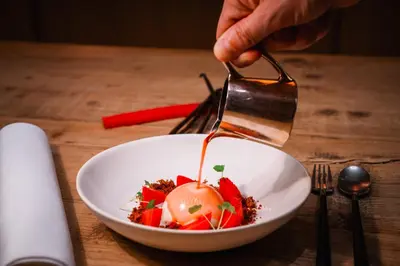 a person is pouring sauce on a bowl of food at Hotel Les Eleveurs in Halle