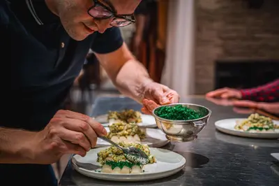 a man preparing food on a table with plates of food at Hotel Les Eleveurs in Halle