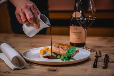 a person pouring sauce on a sandwich on a plate at Hotel Les Eleveurs in Halle