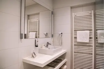 a white bathroom with a sink and a mirror at Hotel Les Eleveurs in Halle