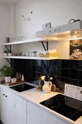 a kitchen with white cabinets and a black tiled wall at Modern Cityflat at Theaterdistrict in Antwerp