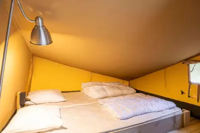 a bed in a yellow room with two pillows at Verblijfpark Tulderheyde in Poppel