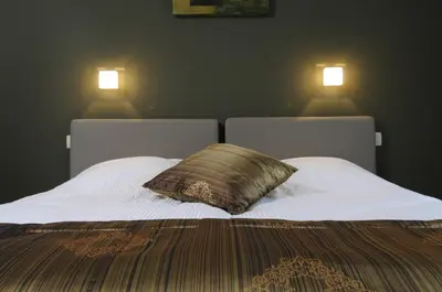 a bed with a pillow and two lights on the wall at Gastenhof Ter Lombeek in Onze-Lieve-Vrouw-Lombeek