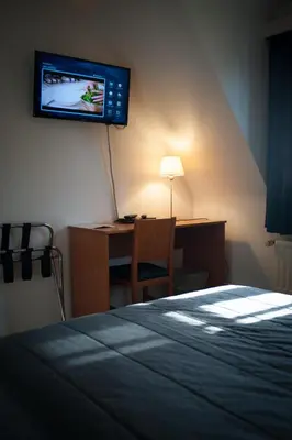a bedroom with a bed and a desk with a television on the wall at JFK Hotel Zelzate - Gent in Zelzate