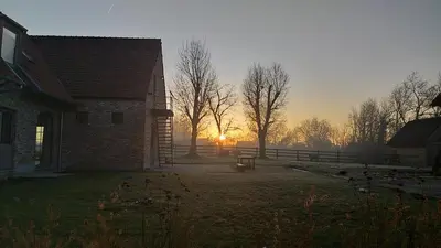 a sunset behind a house with a bench in a yard at Muntershof in Velzeke-Ruddershove
