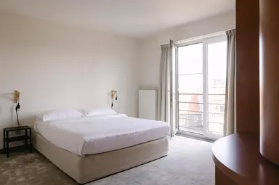 a white bedroom with a bed and a large window at Verac Flats in Zaventem