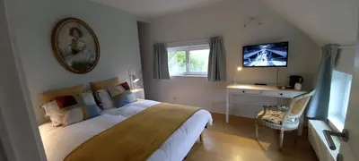 a bedroom with a large bed and a tv on the wall at little cottage in Lasne