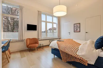 a bedroom with a bed and a desk and two windows at Borgerhouse B&B in Antwerp