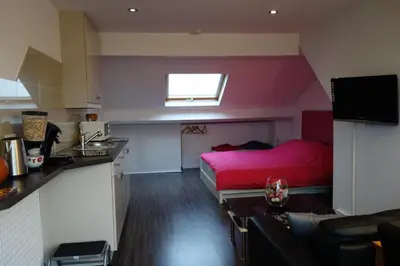 a small room with a red bed and a kitchen at B&B Basilique in Brussels