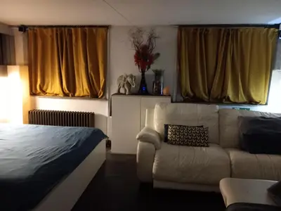 a bedroom with a bed and a couch and yellow curtains at nice and cosy place with jacuzzi and sauna to relax in the centre of antwerp in Antwerp