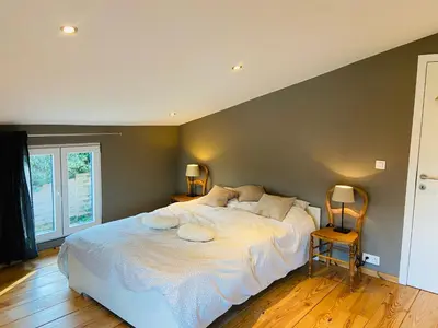a bedroom with a large white bed and a chair at Jolie maison avec jardin. in Hoeilaart