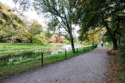 a park path next to a fence and a river at Casa Plantin with parking place at the beautiful city park! in Antwerp