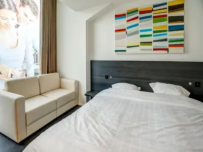 a woman standing in a bedroom with a bed and a couch at Apartment in Weelde with swimming pool in Weelde