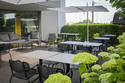an outdoor patio with tables and chairs and umbrellas at Hotel Essenza in Puurs