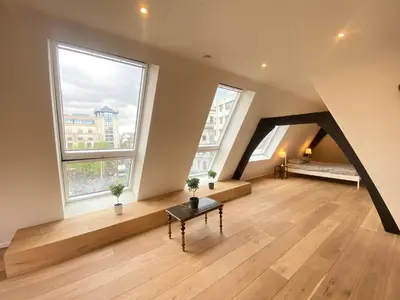 an attic room with a bench and two windows at The Central Square Residence in Antwerp