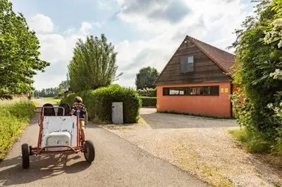 a child riding a cart in front of a house at Vakantiehuis Wandelen en fietsen in de Kalkense Meersen dichtbij Gent in Laarne
