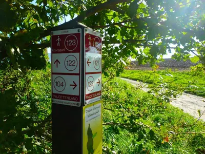 a sign with arrows on a pole next to a tree at Het Verblijf in Sint-Martens-Lennik