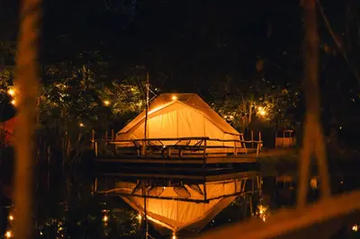a lit up tent on the water at night at AMANI - Aap in Lichtaart