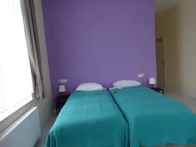 two beds in a room with a purple wall at Hotel de la Gare Aalst in Aalst