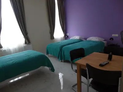 two beds in a room with a table and chairs at Hotel de la Gare Aalst in Aalst