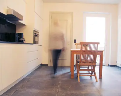 a woman walking through a kitchen with a table and a chair at Dendernachten in Dendermonde