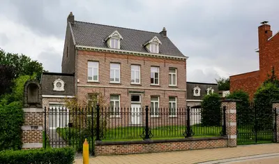 a large brick house with a black fence at Amand'eau - zwemvijver, zonneterras, grote tuin in Sint-Amands