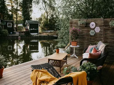 a deck with chairs and a table next to a pond at Geel Chalet in Netevallei in Geel