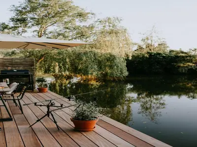 a wooden deck with a table and an umbrella and a lake at Geel Chalet in Netevallei in Geel