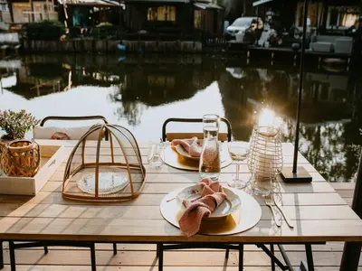 a wooden table with plates of food on it next to the water at Geel Chalet in Netevallei in Geel