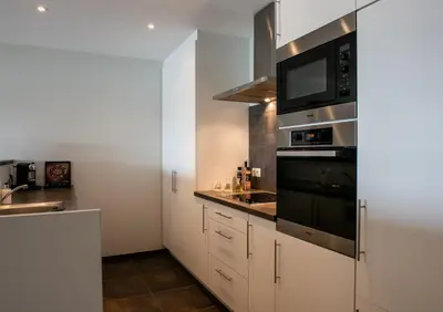 a small kitchen with white cabinets and a microwave at Scheldeoever in Temse
